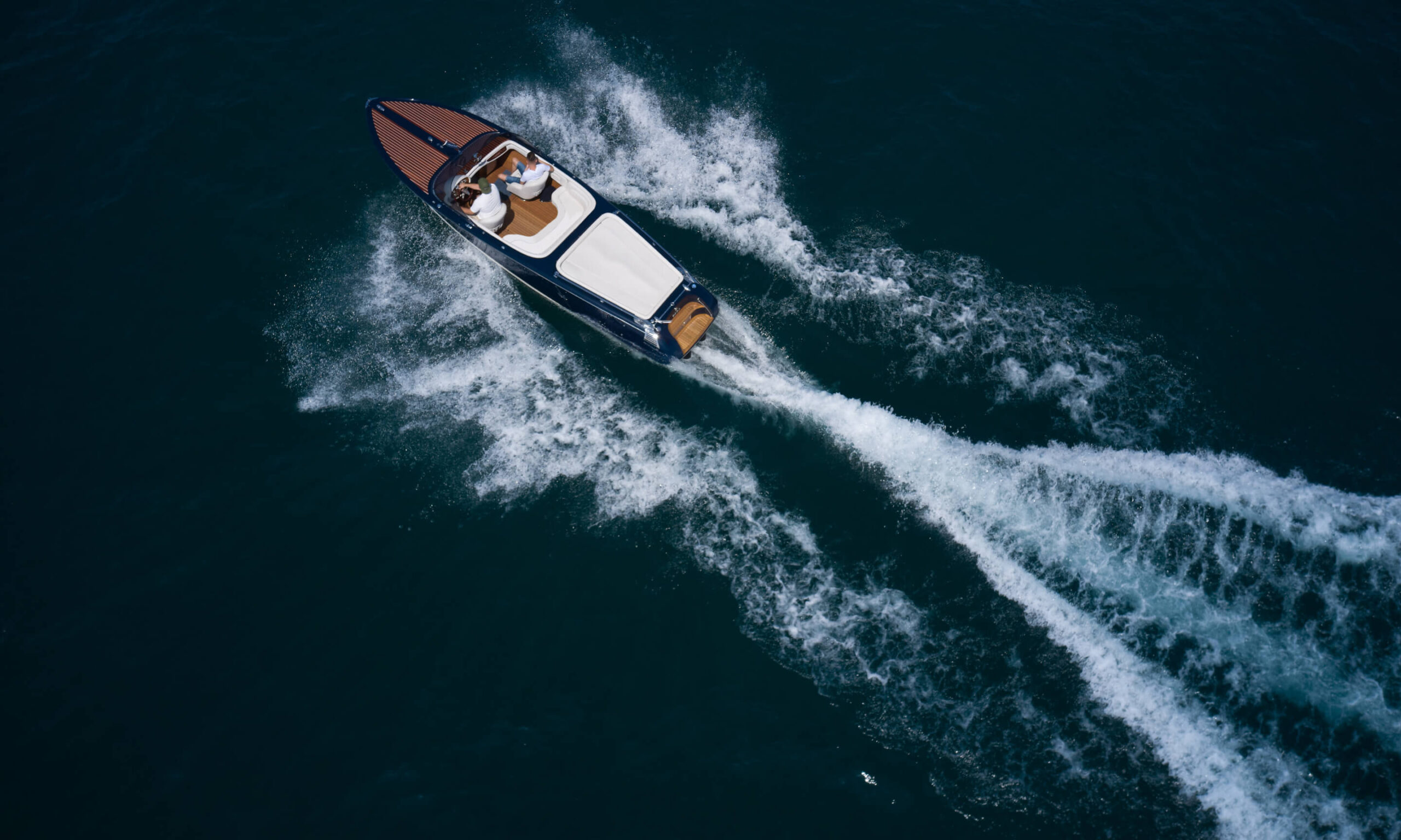 bird eye view of two people riding a luxury wooden runabout yacht in the ocean